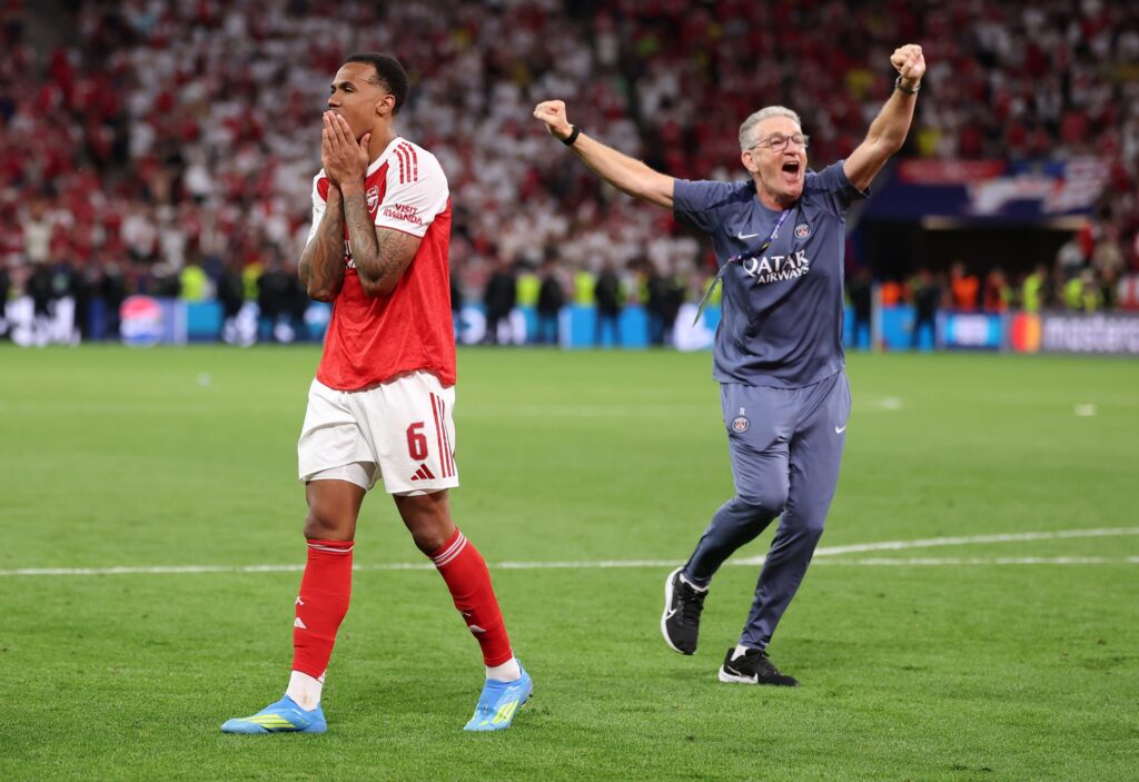 An emotional Arsenal player walks away with hands covering his mouth after a missed penalty while a jubilant PSG coach celebrates in the background during the Champions League final.