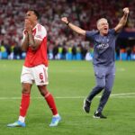 An emotional Arsenal player walks away with hands covering his mouth after a missed penalty while a jubilant PSG coach celebrates in the background during the Champions League final.
