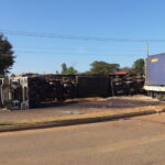 Overturned truck lying on its side across a road after colliding with a freight train at a railway crossing in Bungoma; the train, loaded with cargo containers, is visible on the right side of the image.