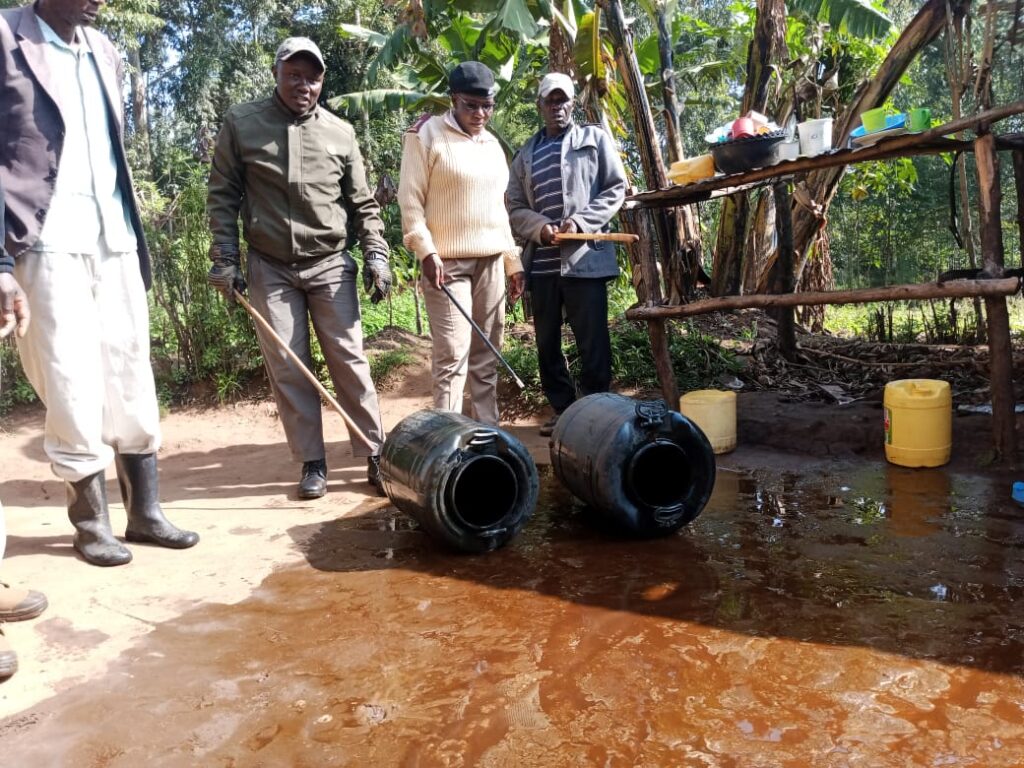 Assistant Chief Joseline Juma stands with village elders as seized containers of illicit brew are destroyed at a homestead in Bituyu A Village, Mbagara Sub-location, Mautuma Ward