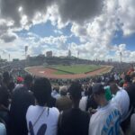 Wide view of a fully packed Nyayo National Stadium in Nairobi with thousands of fans seated around the pitch during a football match, with players visible on the field under a cloudy sky.