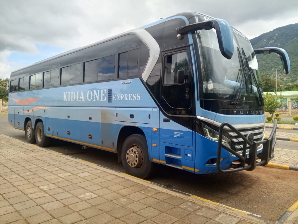 A blue long-distance passenger bus labeled “Kidia One Express” parked by the roadside, linked to an incident where a python was discovered hidden inside a box at Namanga border.