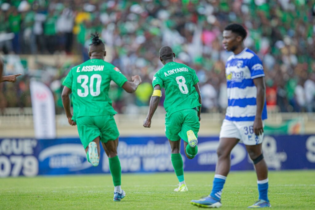 Gor Mahia players in green kits celebrate a goal while an AFC Leopards player in a blue and white kit looks on during a crowded derby match at Nyayo Stadium.
