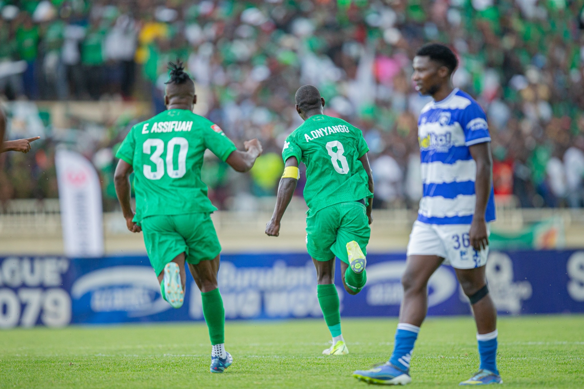Gor Mahia players in green kits celebrate a goal while an AFC Leopards player in a blue and white kit looks on during a crowded derby match at Nyayo Stadium.