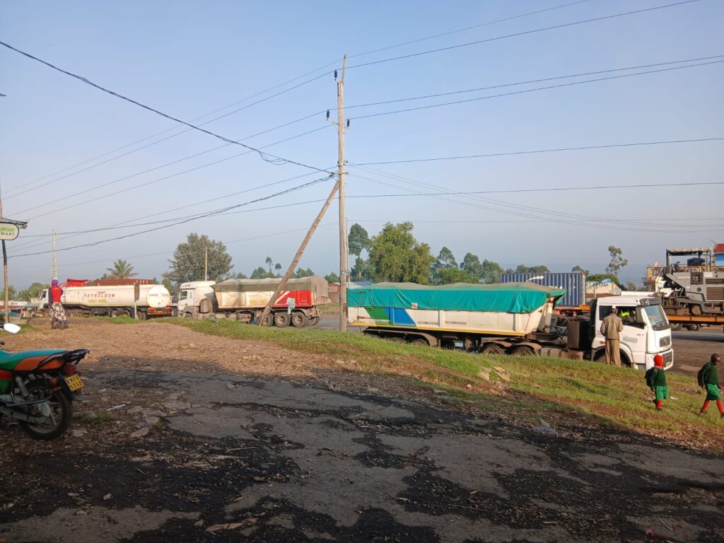 Several cargo trucks parked along a busy roadside near Chimoi Market, with a rough, damaged road surface and pedestrians nearby.