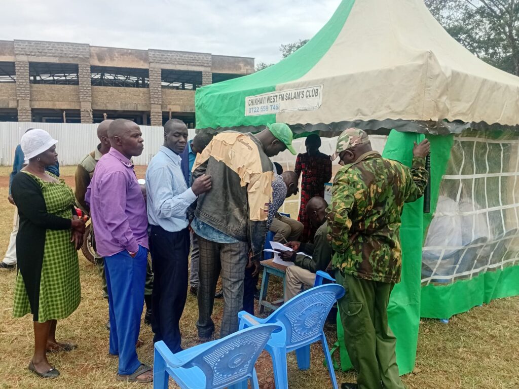 Men and women gather around a small tent where officials check documents and register voters during a local market election exercise at Panpaper Market.
