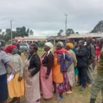 A group of traders, mostly women in aprons and headscarves, stand in a queue outdoors at Panpaper Market in Lugari, waiting to take part in the market leadership election.