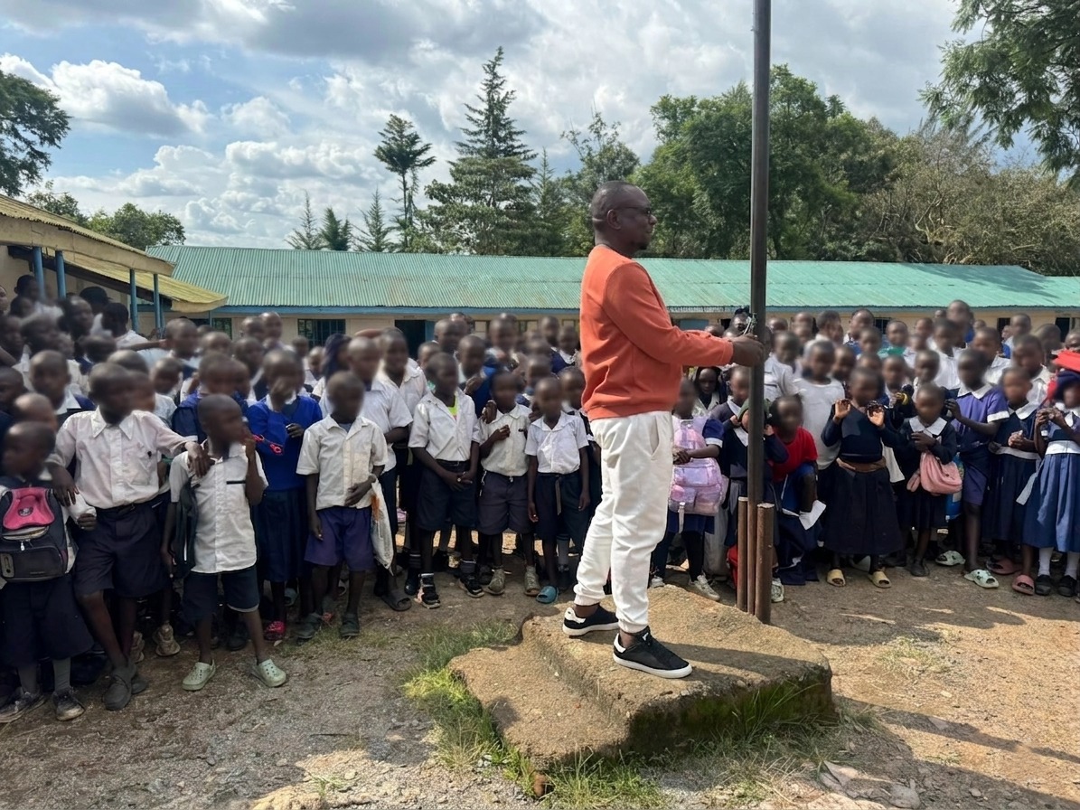 Philip Etale stands in front of a large group of pupils at Munyuki Comprehensive School while speaking during a school event.