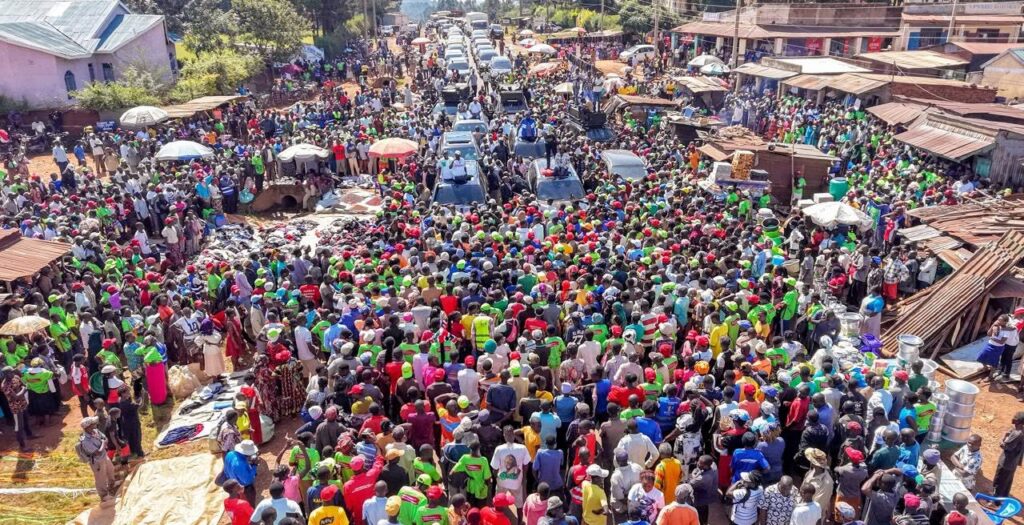 An aerial view of thousands of people lining a busy market road in Vihiga during an opposition political rally, with vehicles moving through the crowd as supporters gather around.
