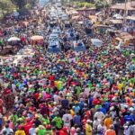 An aerial view of thousands of people lining a busy market road in Vihiga during an opposition political rally, with vehicles moving through the crowd as supporters gather around.