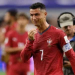 Cristiano Ronaldo of Portugal appears emotional after Portugal's 1-0 loss to Spain in the FIFA World Cup Round of 16, with players and broadcast crew visible in the background.