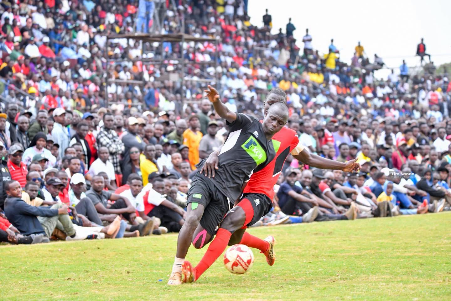 Two players from Kakamega School and St. Mary's School Yala battle for possession during the KSSSA national football final as thousands of spectators watch from the packed stands in Thika.
