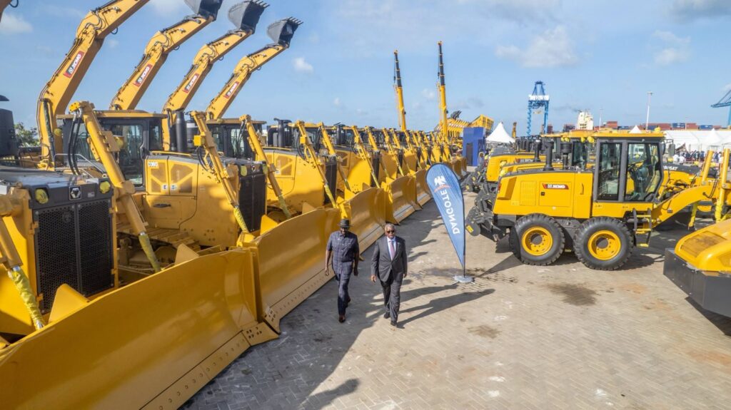 President William Ruto and Aliko Dangote walking between rows of yellow construction machinery at the Dangote refinery groundbreaking ceremony in Lamu.