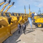 President William Ruto and Aliko Dangote walking between rows of yellow construction machinery at the Dangote refinery groundbreaking ceremony in Lamu.